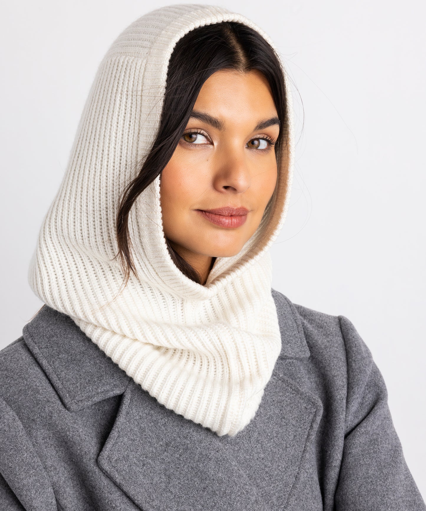 Model is wearing the ivory Perfect Ribbed Balaclava and a grey pea coat.  She is softly smiling and one piece of hair wisps out from under the balaclava. 